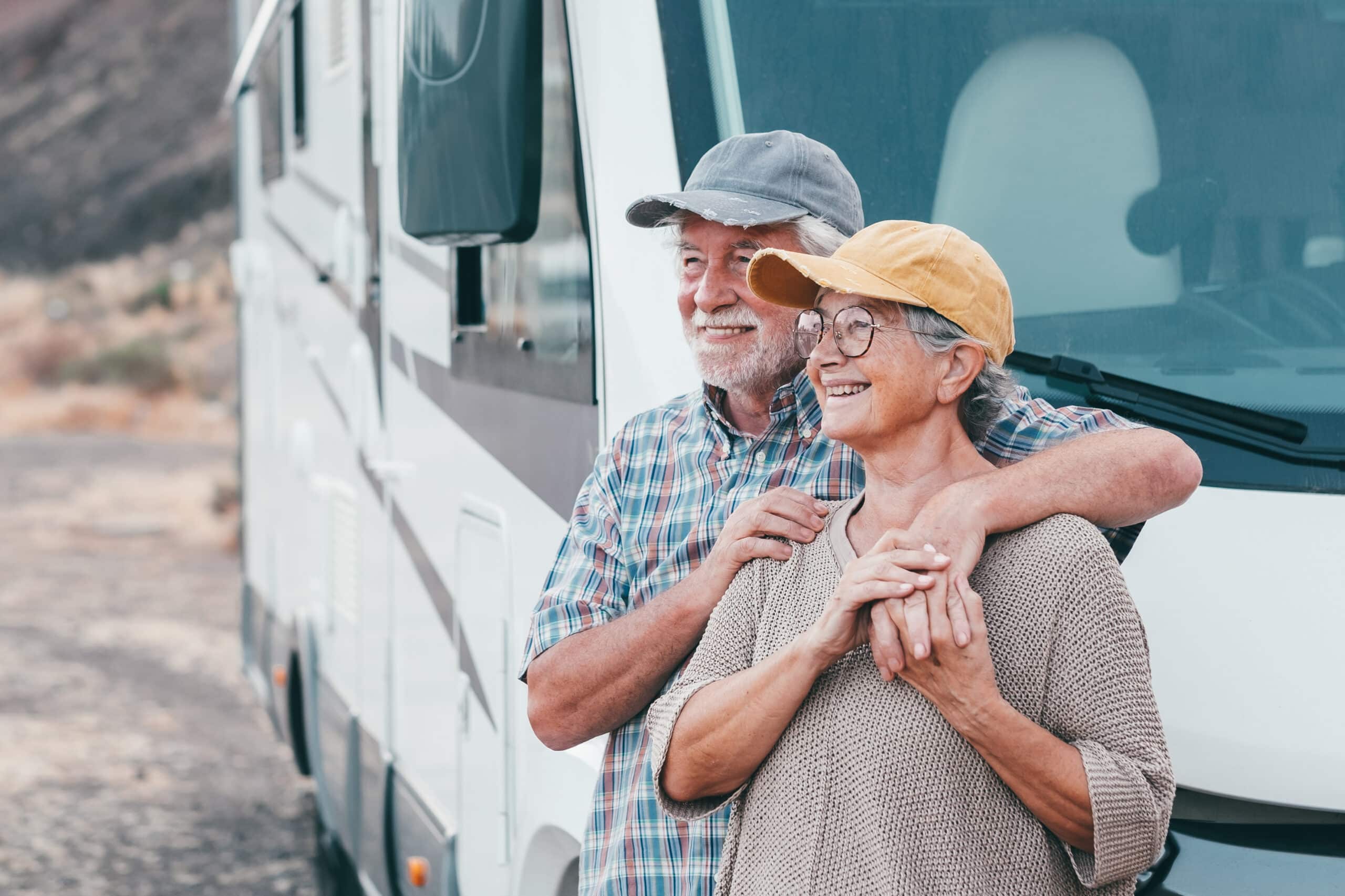 Happy senior couple on leisure trip enjoying travel destination standing outside a camper van motorhome hugging looking away. Smiling elderly man and woman, transport and tourism concept lifestyle