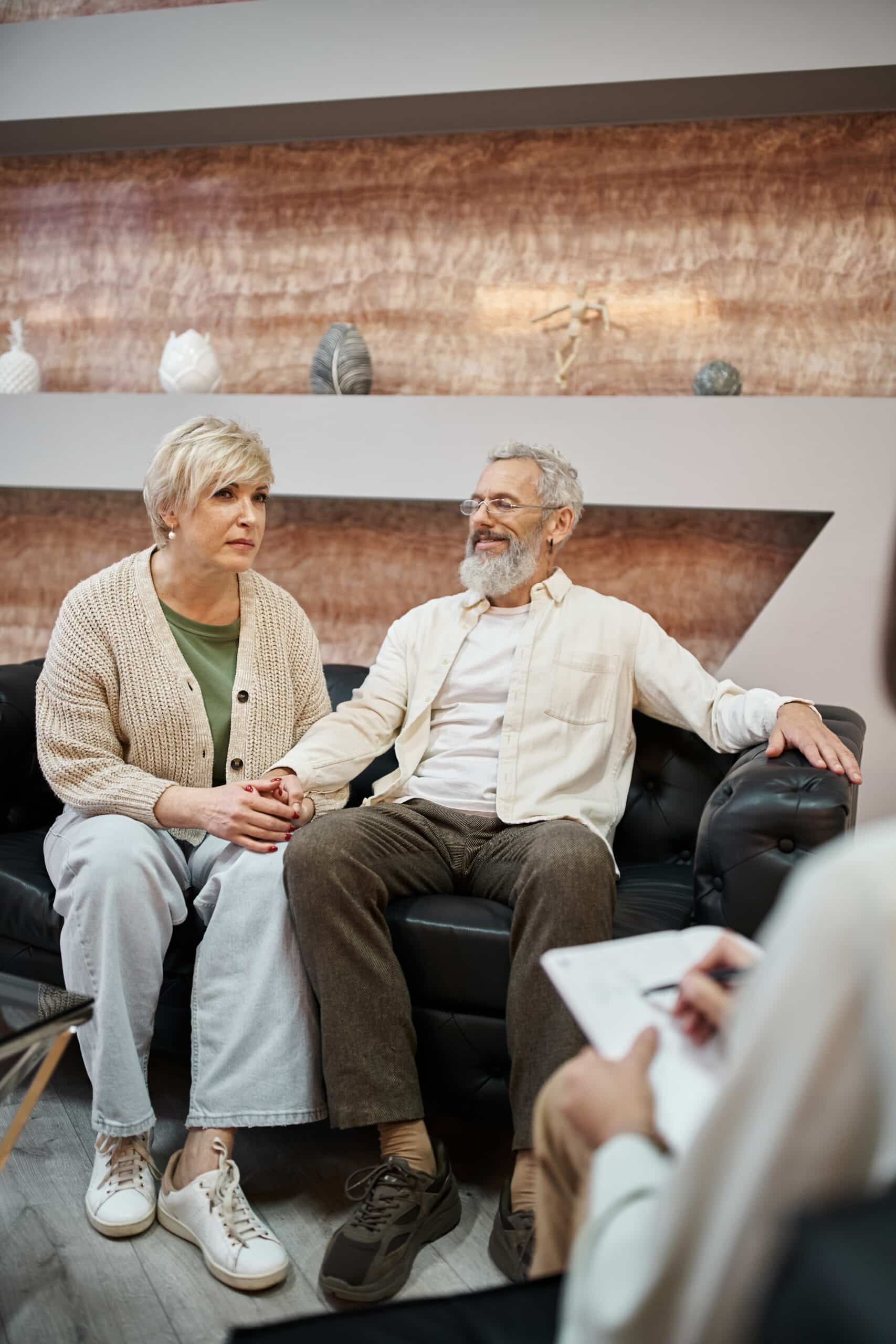 middle aged married couple sitting on leather couch near psychologist taking notes during consult