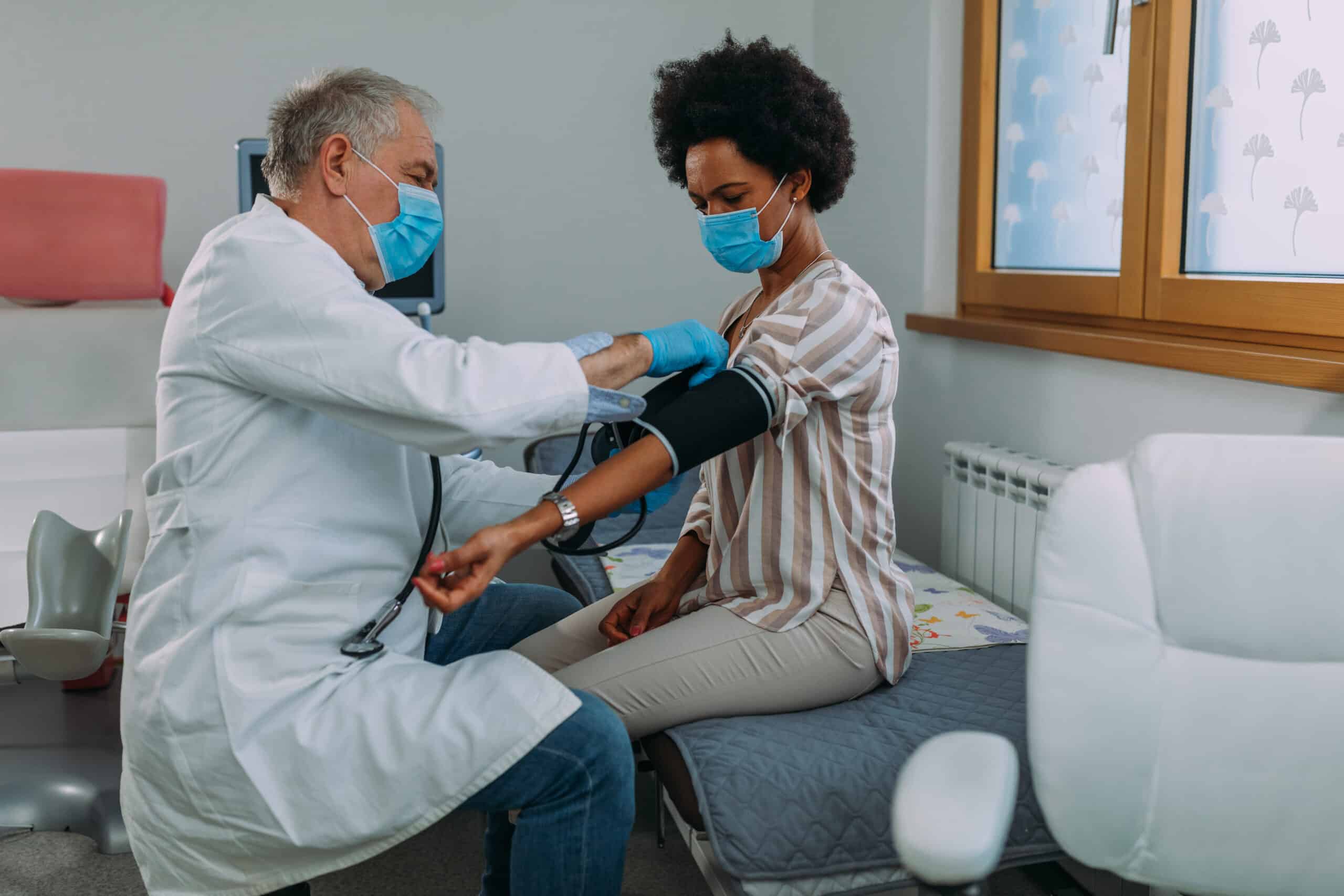 Doctor with face mask measures blood pressure to the patient at hospital office